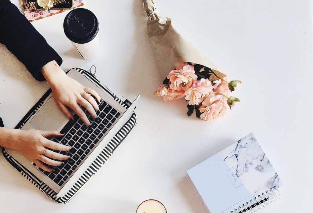 hands on white table typing on a computer next to pink flowers