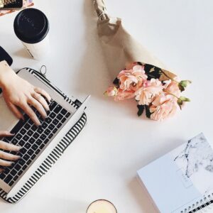 hands on white table typing on a computer next to pink flowers